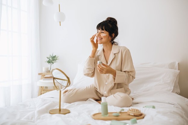 woman sitting on bed doing self care on her face for the manzanilla sophia blog